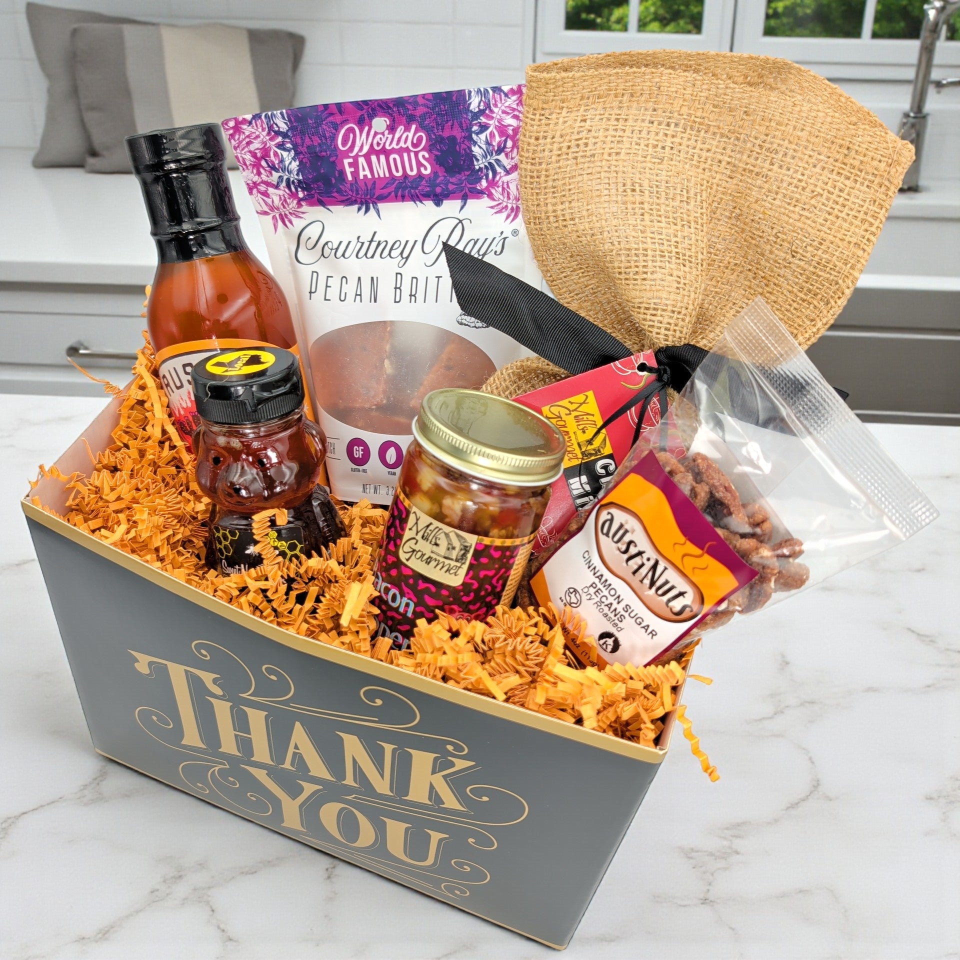 Gift basket with various items including a bottle, jar, and a hat on a marble surface, sourced with Texas-made goods