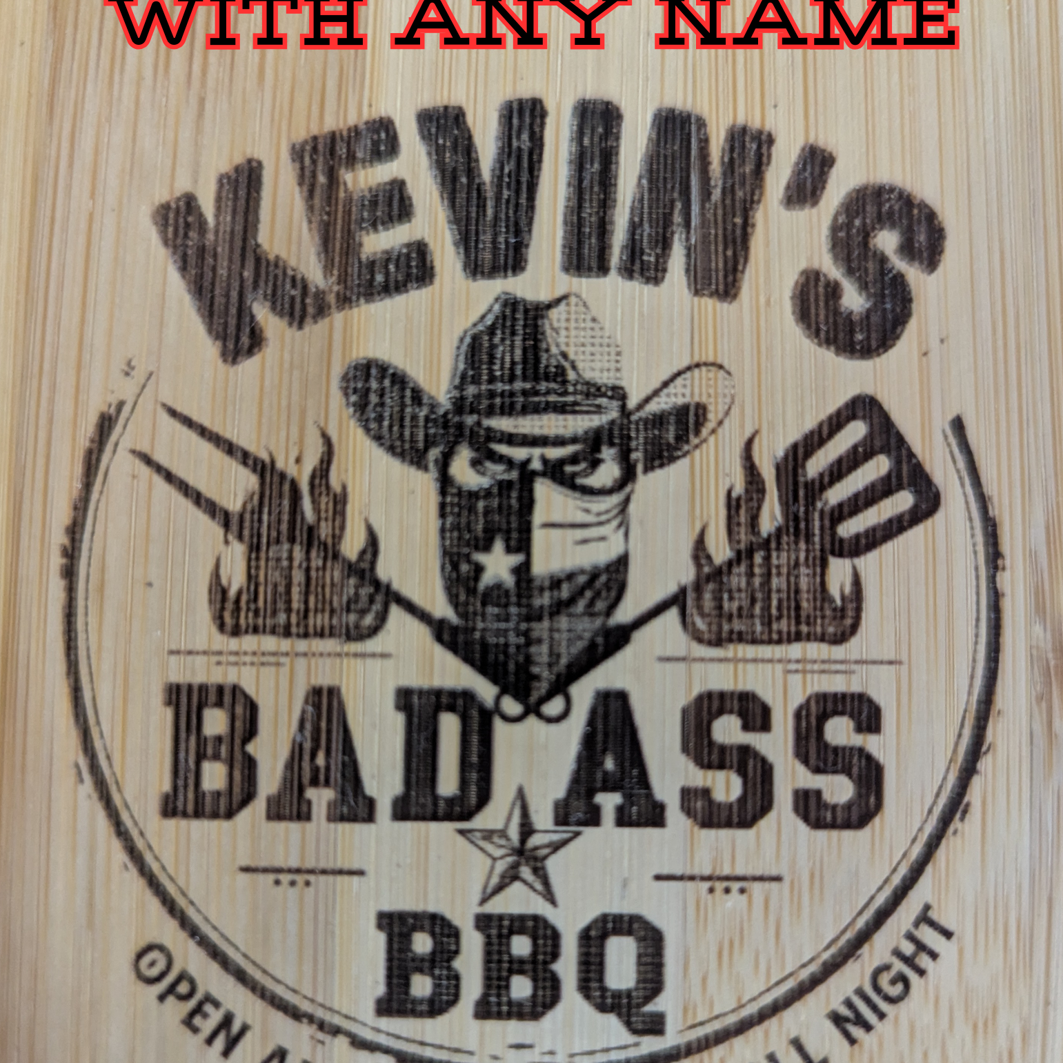 Close-up of an engraved bamboo grill scraper showing a customizable “Bad Ass BBQ” design with a masked cowboy, crossed grilling tools, and bold text indicating personalization with any name.