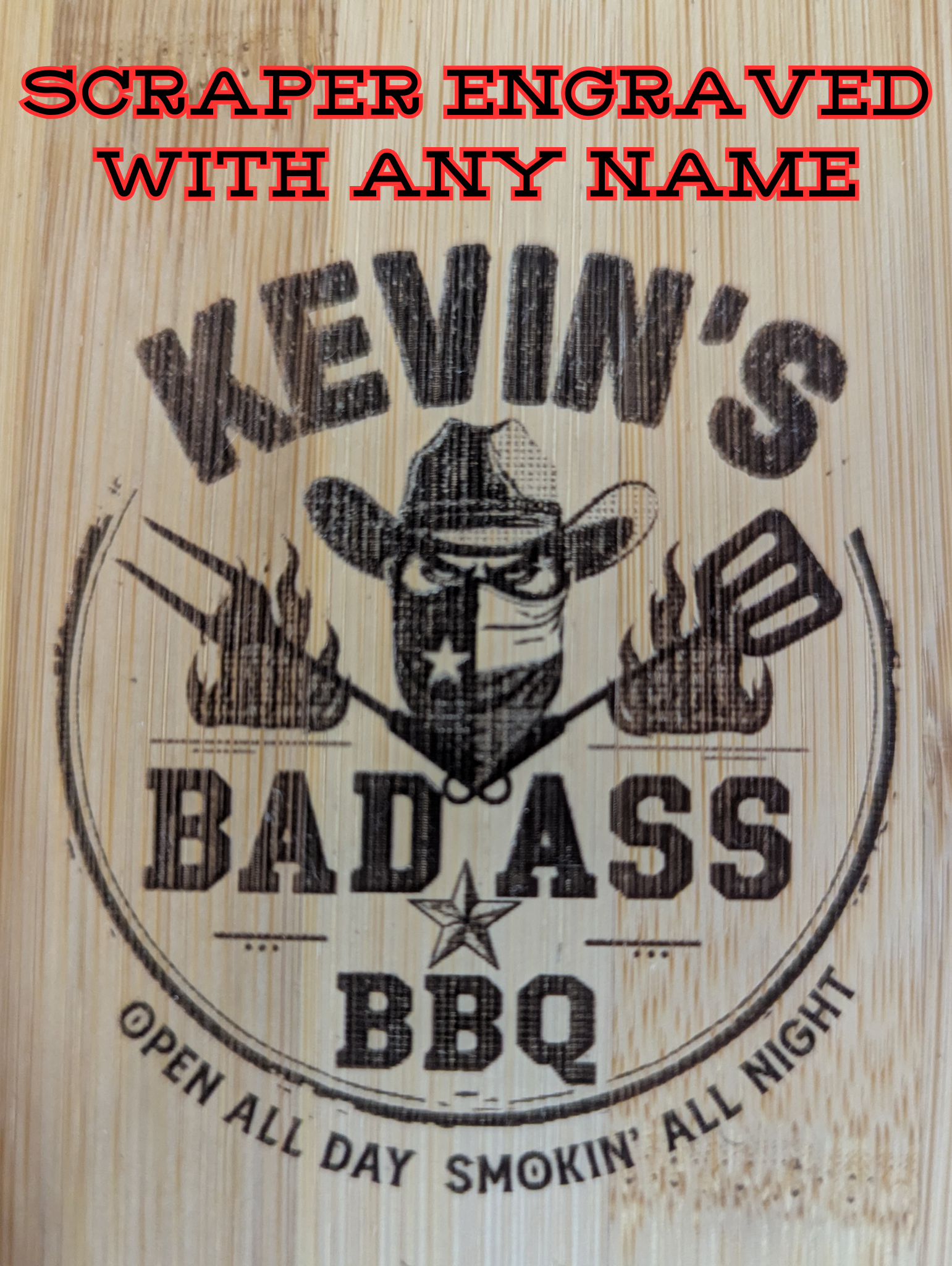 Close-up of an engraved bamboo grill scraper showing a customizable “Bad Ass BBQ” design with a masked cowboy, crossed grilling tools, and bold text indicating personalization with any name.