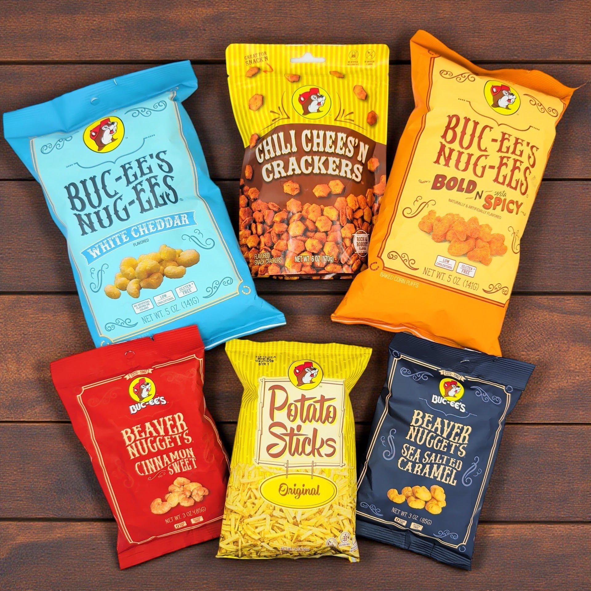 an assortment of six bucees snacks, including white cheddar beaver nuggets, chili cheese n crackers, bold n spicy nuggets, cinnamon sweet beaver nuggets, potato sticks, and sea salted caramel beaver nuggets