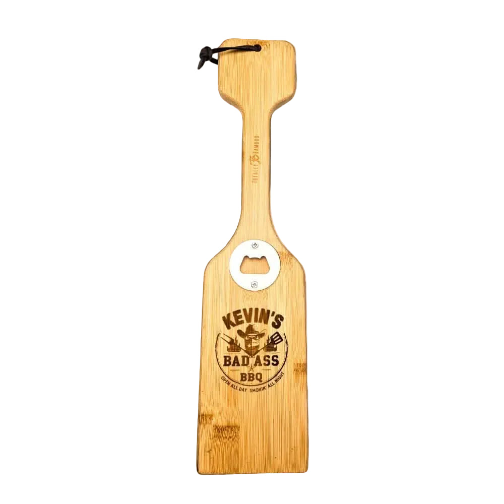 Personalized bamboo grill scraper with a built-in metal bottle opener, engraved with “Kevin’s Bad Ass BBQ” logo, isolated on a white background.