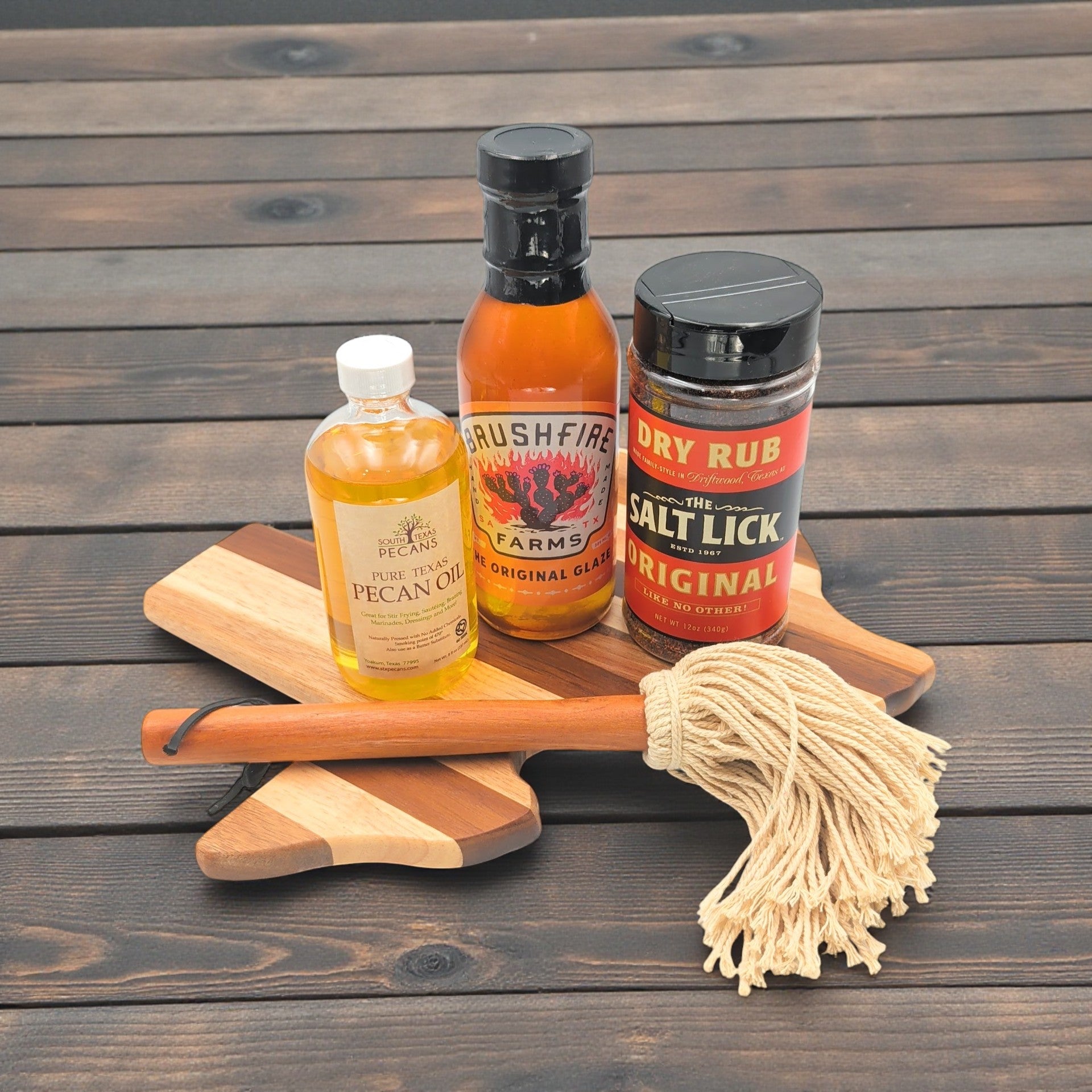 Assorted texas bbq products including a bottle of glaze, bottle of pecan oil,, bbq sauce, and cutting board on a wooden surface, optimal texas gift