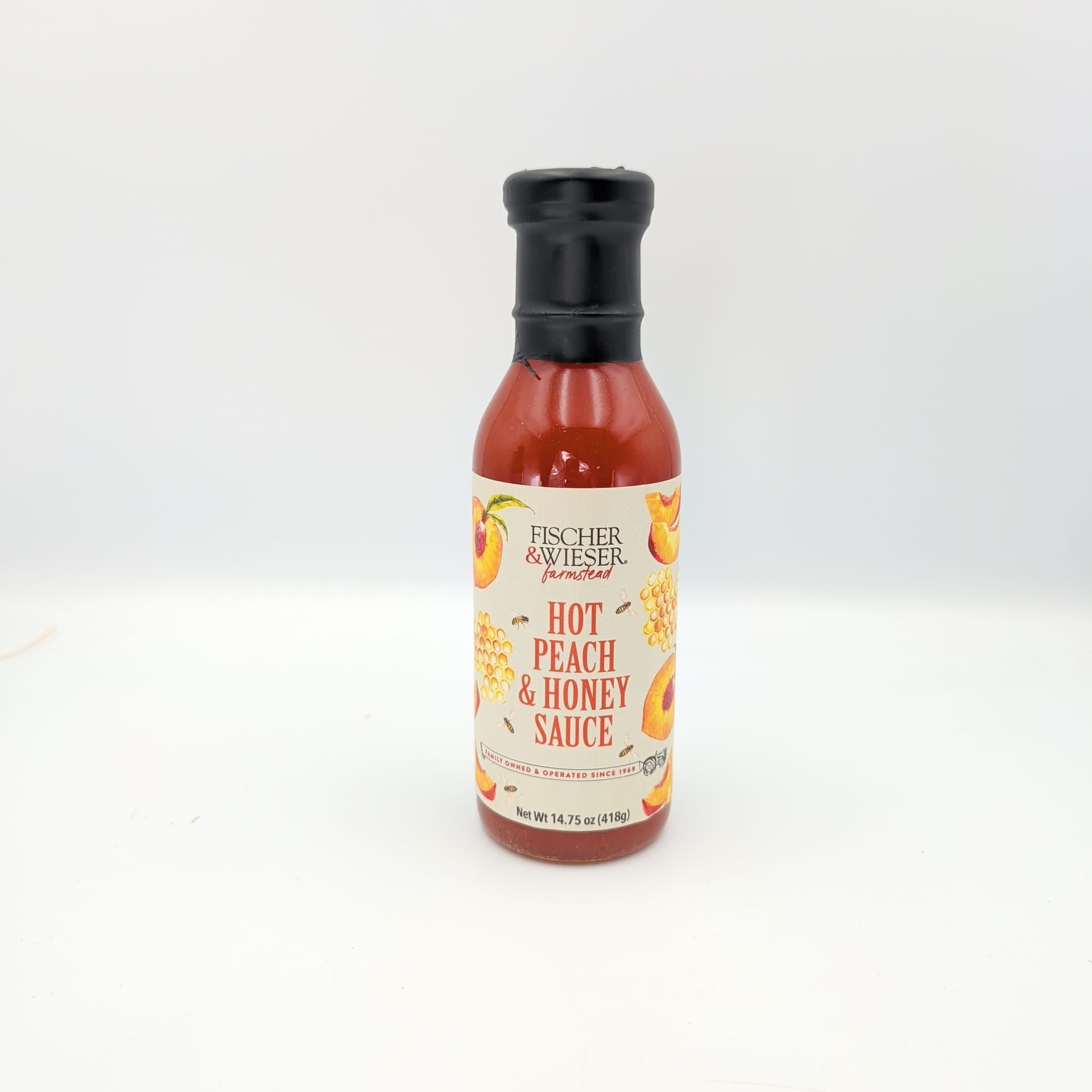 Gourmet hot peach and honey sauce in a glass bottle with fruit-inspired label artwork, displayed on a white background for Texas gift baskets and specialty food collections.
