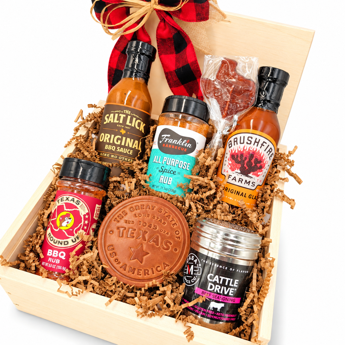 Angled close-up of Texas Pitmaster Pantry showing five barbecue sauces and seasonings, a Texas leather coaster and lollipop on white.