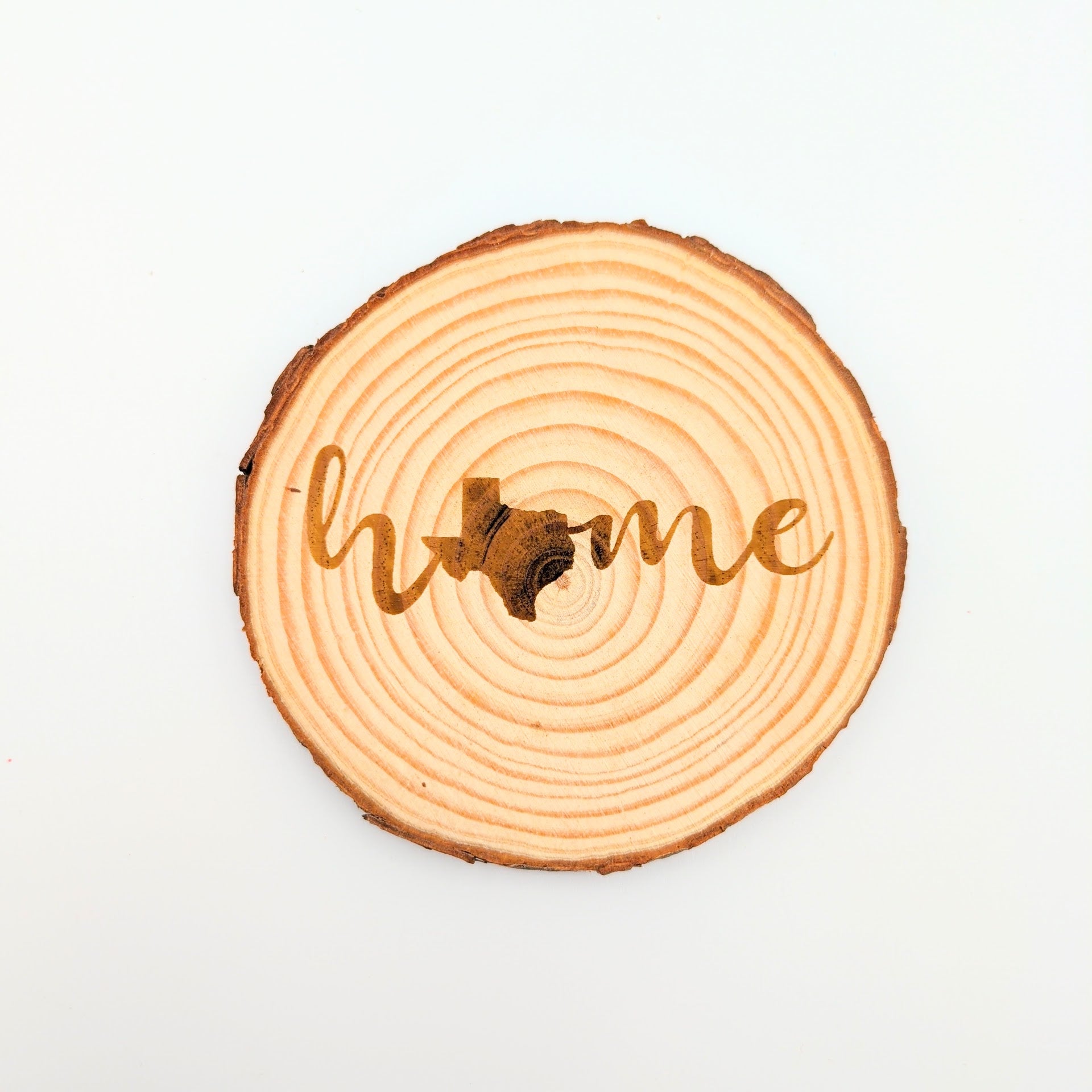 Wooden circular coaster with 'home' engraved on a white background, with a Texas silhouette