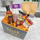 Gift basket with various items including a bottle, jar, and a hat on a marble surface, sourced with Texas-made goods