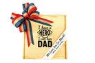 Personalized wooden gift box featuring the phrase “I have a hero I call him Dad,” decorated with a red, blue, and gold ribbon bow and a custom message ribbon reading “We Love You So Much,” presented as a Father’s Day gift.