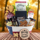 Houston Home Breakfast Basket with rustic background, Texas-themed tin filled with pecan coffee, cinnamon roll mix, jalapeño cornbread mix, granola, honey, praline, and preserves.