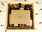 Open wooden gift box filled with Texas-made gourmet items, including infused olive oil, jam, seasoning, and sweets, topped with a personalized kraft card addressed to Emily, arranged with shredded paper filler and Texas flag confetti.