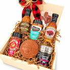 Angled close-up of Texas Pitmaster Pantry showing five barbecue sauces and seasonings, a Texas leather coaster and lollipop on white.